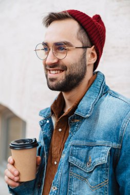 Yakışıklı, mutlu, şık, sakallı bir adamın sokakta elinde kahve fincanıyla dolaşması.