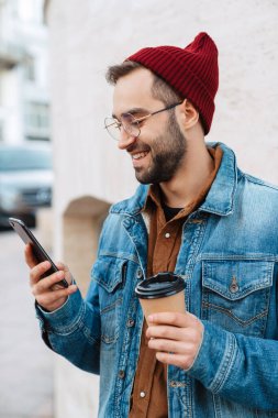Yakışıklı, mutlu, şık, sakallı bir adamın sokakta yürürken elinde kahve fincanı, cep telefonu...