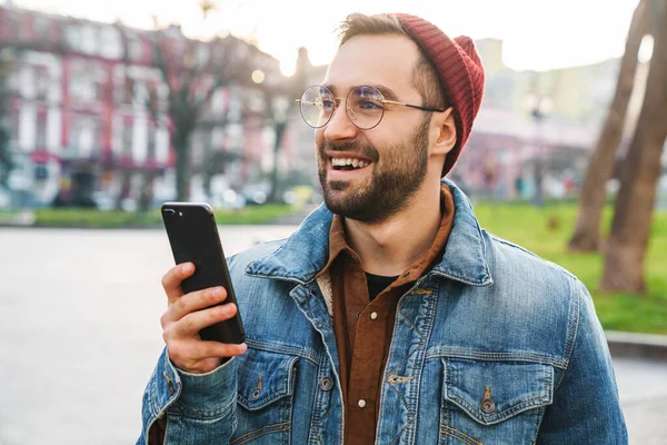 携帯電話を使用して 路上で屋外に歩いてハンサムな幸せな若いスタイリッシュなひげを生やした男の閉じる — ストック写真