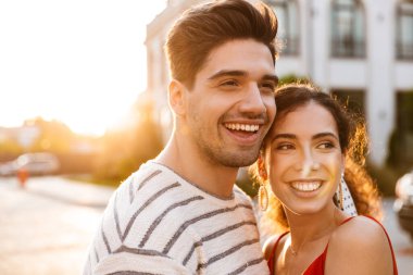 Şehir caddesinde yürürken gülen ve kucaklaşan yaz kıyafetleri içinde mutlu romantik çiftin görüntüsü.