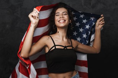 Dövmeli, kameraya gülümseyen ve siyah arka planda izole edilmiş Amerikan bayrağını tutan beyaz bir kadın.