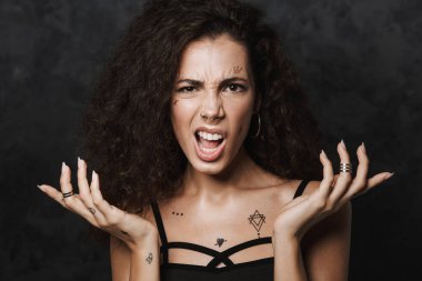 Dövmeli genç bir kadın resmi. Kameraya bakıyor ve siyah arka planda izole edilmiş elleri kusuyor.