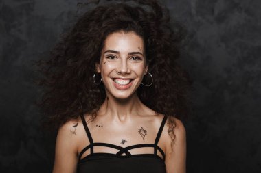 Dövmeli, gülümseyen ve siyah arka planda izole edilmiş kameraya bakan neşeli bir kadın resmi.