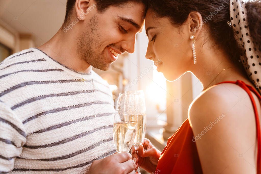 Image closeup of happy young couple standing head to head and drinking champagne near colonnades