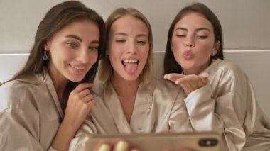 Neşeli, komik, genç kız arkadaşlar, ışık odasındaki cep telefonunda selfie çekerken suratlarını buruşturuyorlar.