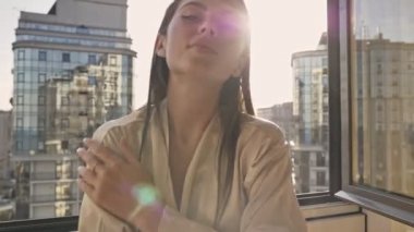 Çekici bir genç kız açık pencerenin yanında duruyor ve kamerayı zehirliyor.