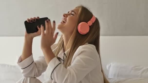 Egy Vonzó Fiatal Boldog Pizsamában Hallgatja Zenét Mobiltelefonnal Fejhallgatóval Miközben — Stock videók