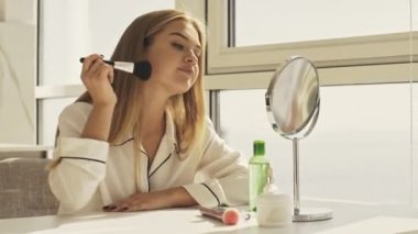 Pijamalı mutlu bir kadın, parlak bir odada otururken toz fırçası kullanıyor ve gülümsüyor.