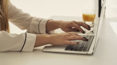 Genç bir kadının ellerinin yakın çekim görüntüsü sabahleyin mutfaktaki bilgisayarında daktilo ediyor.