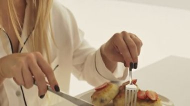 Mutlu sarışın bir kadın, pijamasını giymiş, kahvaltı yapıyor ve masasında otururken gülümsüyor.