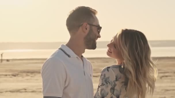 陽気なカジュアルな服のカップルが日当たりの良いビーチを歩いています — ストック動画