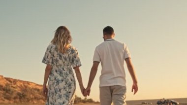 Güneşli sahilde, göl kenarında el ele tutuşurken, günlük giysiler içinde güzel genç bir çiftin arka görüntüsü...