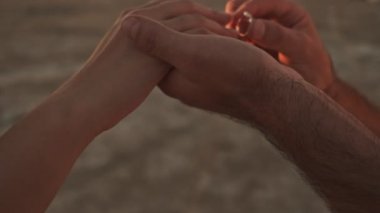 Adam göl kenarındaki güneşli sahilde bir kadına yüzük takarken kesilen eller.