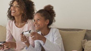 Neşeli Afrikalı kadın ve onun neşeli küçük güzel kızı evde yataktayken joysticklerle oynuyorlar.