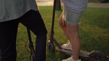 Çekici genç bir çift park alanında elektrikli scooter kullanırken konuşuyor.