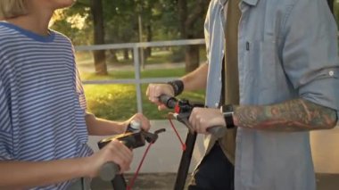 Çekici erkek ve kız gün batımında yeşil park manzarasında yan yana dururken gülüyor ve konuşuyorlar.