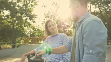 Çekici, mutlu genç bir çift spor alanında elektrikli scooter kullanırken konuşuyor.