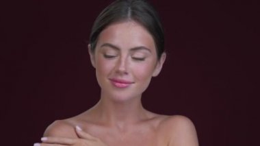 Güzel genç bir kadın kameraya poz veriyor. Koyu kırmızı arka planda izole edilmiş.