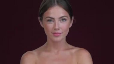 Mutlu, gülümseyen genç bir kadın kafasını sallıyor koyu kırmızı arka planda izole bir şekilde.