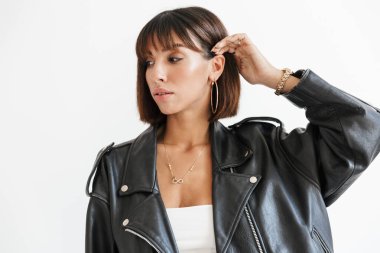 Deri ceket giyen genç ve güzel bir kadın beyaz arka planda yalnız duruyor.