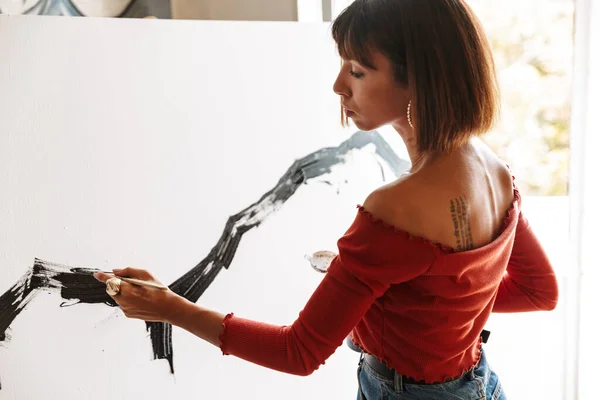 スタジオで絵を描きながら絵画ツールを使用した若い白人芸術家女性の肖像画 — ストック写真