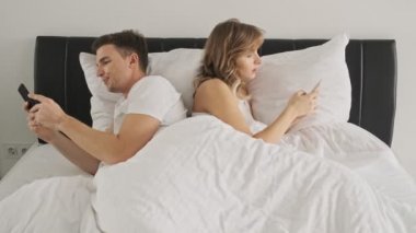 Odaklanmış bir çift cep telefonlarını kullanarak sırt sırta yatıyorlar.