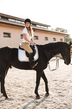 Beyaz tenli, ciddi, sarışın, güzel bir kadının kırsalda at şapkası taktığı bir fotoğraf.