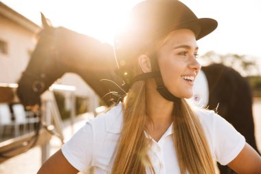 Gülümseyen mutlu genç bir kadının kırsalda at şapkası taktığı görüntüsü.