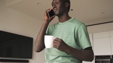 İyi görünümlü Afro-Amerikan bir adam evinde dinlenirken akıllı telefonuyla konuşuyor.