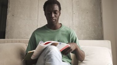 Sakin, ciddi, Afro-Amerikan bir adam, günlük giysiler içinde oturma odasında egzersiz yaparken gözlüğünü takıyor.