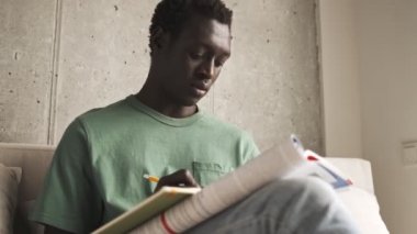 Sakin bir Afrikalı Amerikalı günlük giysiler içinde ev ödevini oturma odasında yapıyor.