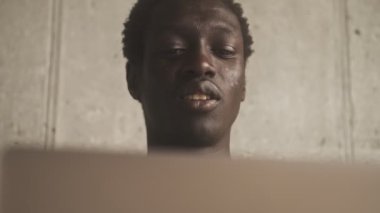 Çekici bir Afrikalı Amerikalının yakın plan görüntüsü oturma odasında oturan gümüş dizüstü bilgisayarını kullanıyor.