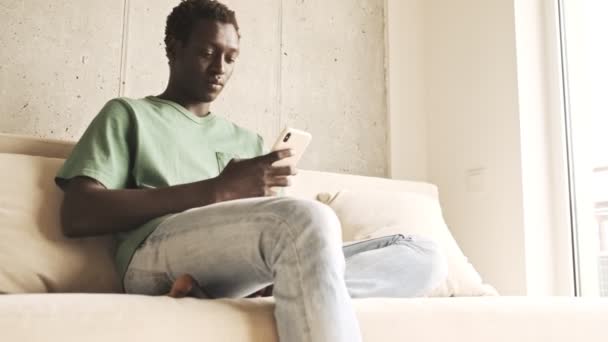 Poniżej Widok Spokojnego Afrykańskiego Mężczyzny Luźnych Ubraniach Używa Smartfona Siedząc — Wideo stockowe