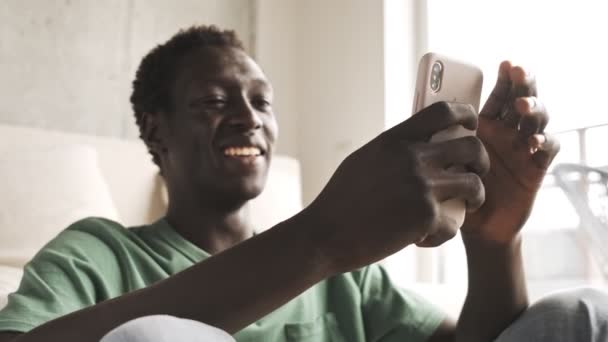 Hombre Afroamericano Risueño Feliz Está Viendo Algo Teléfono Inteligente Sala — Vídeos de Stock