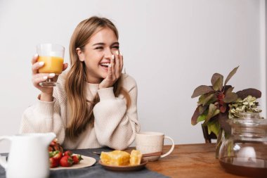Rahat bir odada kahvaltı ederken günlük giysiler içinde gülen mutlu beyaz kadın görüntüsü.
