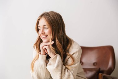 Beyaz arka planda izole bir şekilde, koltukta otururken gülümseyen rahat genç kadın görüntüsü