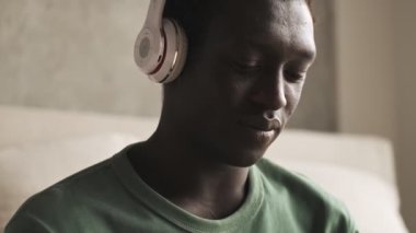 Kablosuz kulaklıklı sakin, genç bir Afrikalı Amerikalı adamın yakından görüntüsü evdeki oturma odasında müzik dinliyor.