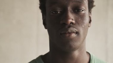 Sakin, genç, Afro-Amerikan bir adamın yakın çekim görüntüsü oturma odasındaki kameraya bakıyor.