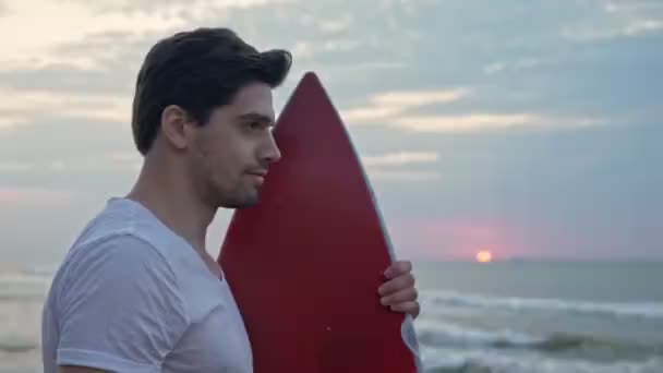 站在海边与冲浪板站在一边笑着的英俊男子的侧影 — 图库视频影像