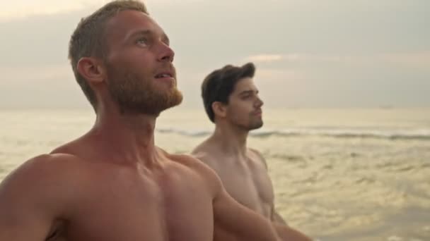 海の近くのビーチでヨガの練習をしている2つの濃縮された筋肉ハンサーサーファー — ストック動画