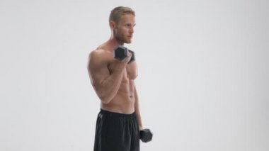 Çekici, genç, kaslı, üstsüz bir sporcu beyaz arka planda tek başına duran ağır halterleri kaldırıyor.