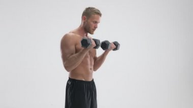 Güçlü, çekici, genç, kaslı, üstsüz bir sporcunun beyaz arka planda izole bir şekilde duran ağır halterleri kaldırışının yan görüntüsü.