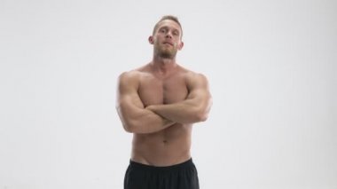 Kendinden emin, genç, üstsüz bir sporcu ellerini çapraz yapıp beyaz arka plan üzerinde duruyor.