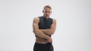 Ciddi bir genç sporcu beyaz arka planda izole edilmiş tişörtünü çıkarıyor.