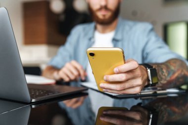 Evdeki kithcen 'de dizüstü bilgisayarda çalışırken cep telefonu kullanan konsantre bir gencin fotoğrafını çek.