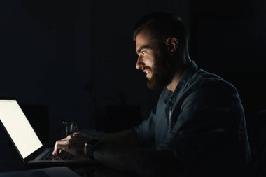 Geceleri masada otururken dizüstü bilgisayarda çalışan kendine güvenen genç adam.