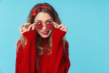 Güneş gözlüklü neşeli beyaz kadın görüntüsü. Yan bakıyor ve mavi arka planda izole bir şekilde gülümsüyor.