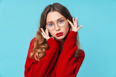 Gözlüklü beyaz kadının görüntüsü mavi arka planda izole edilmiş kameraya bakıyor ve poz veriyor