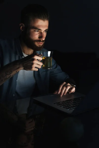 Уверенный Себе Молодой Человек Работающий Ноутбуком Сидя Столом Помещении Ночью — стоковое фото