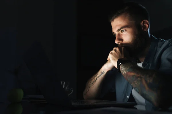Magabiztos Fiatalember Dolgozik Laptop Számítógép Miközben Asztalnál Beltéri Éjszaka — Stock Fotó